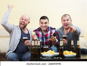 Three Male Sport Fans Watching Hockey Game Heatedly In Livingroom