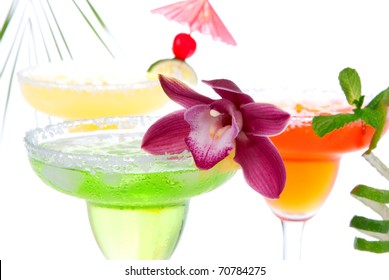 Three Margaritas Cocktails Composition Decorated With Lime, Orchid, Cherry, Apple, Peach And Drink Umbrella In Margarita Glasses  Isolated On A White Background