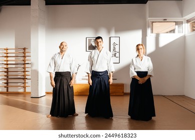 Three martial arts instructors stand with poise in a well-lit dojo, exuding confidence and discipline in their traditional attire looking at camera (Text meaning: "Aikido"). - Powered by Shutterstock