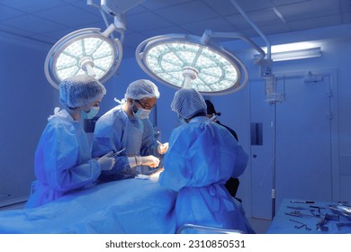 Three medical surgeons in scrubs and one standing at the head of the patient in dark blue scrubs are operating a surgery and talking - Powered by Shutterstock