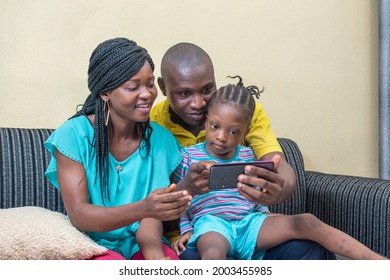 
A three member family curdled and sitting together on a sofa with a mobile smartphone in their hands, the group consist of a little African girl, woman and a man 