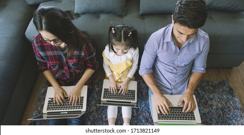 Three Members Of Diverse Family, Caucasian Father And Asian Mother And Little Half Daughter Sitting Together In House Living Room And Using 3 Laptop Notebook Computers. Idea For Working At Home.