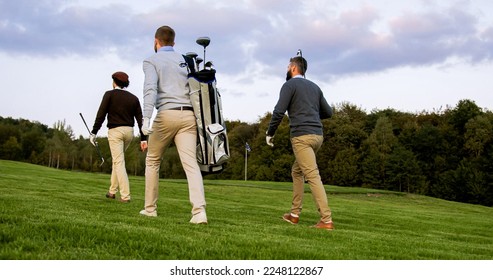 Three men with clubs and golf bag walking on the golf fied. Back view from below. Outside - Powered by Shutterstock