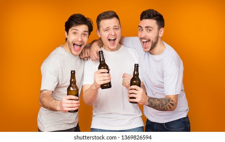 Three Men Holding Beer Bottles And Celebrating Meeting Over Orange Studio Background