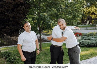 Three men hug each other in a park. Scene is warm and friendly. The men are dressed in formal attire, which suggests that they might be attending a special event or gathering - Powered by Shutterstock