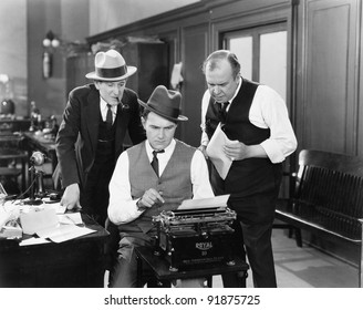 Three men in an office hunched over a typewriter