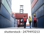 Three men in safety vests walk through a large container yard. The men are wearing yellow vests and are walking in a line