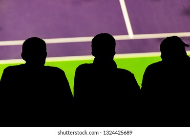 Three Men Are Seen From Behind, Looking At The Tennis Court With The View Of The Purple With Green Court In The Background