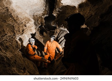 Three men, strong physique, explore the cave. Men dressed in special clothes to pass through the cave and stopped, looking at the map.