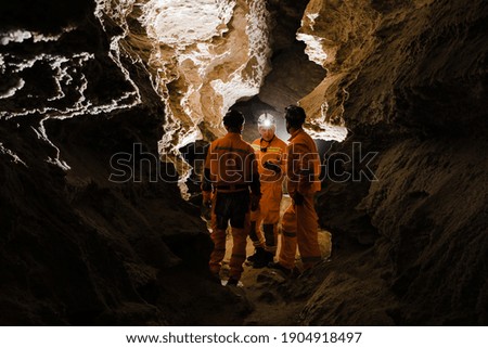 Three men, strong physique, explore the cave. Men dressed in special clothes to pass through the cave and stopped, looking at the map.