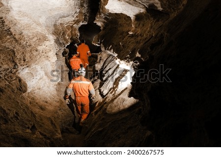Three men, strong physique, explore the cave. Men dressed in special clothes to pass through the cave and stopped, looking at the map.