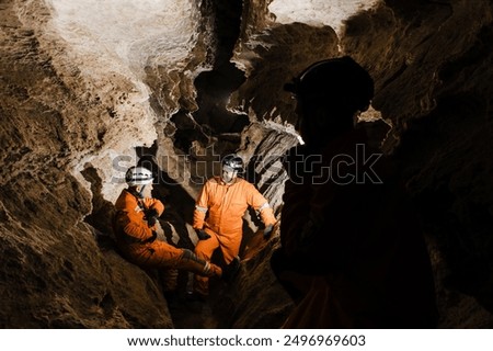 Three men, strong physique, explore the cave. Men dressed in special clothes to pass through the cave and stopped, looking at the map.