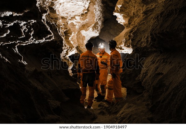 Three men, strong physique, explore the cave. Men\
dressed in special clothes to pass through the cave and stopped,\
looking at the map.