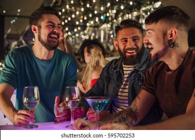 Three Men Are Talking And Laughing While Enjoying Drinks In A Night Club. 