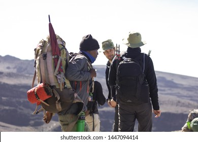 Three Men Walking On The Mountain Trek, Have A Lot Of Equipment For The Climbing To The Top Of Kilimanjaro. Dangerous Trip, Strong And Sport People. Comfortable And Warm Clothes, Backpacks On The Back