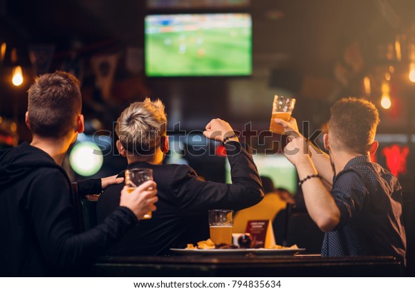 Three men\
watches football on TV in a sport\
bar
