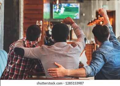 Three Men Watching Football On TV In Sport Bar, Back View