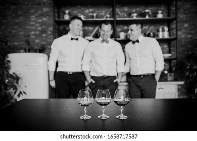 Three Men In A White Shirt Drink Whiskey In Glasses In A Loft Apartment