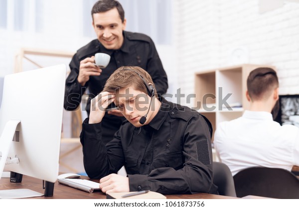 Three men\
work in the security room. Two of them are dressed in uniform. The\
men are sitting in front of the\
monitors.
