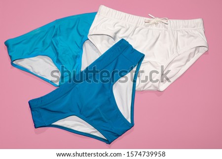 Three men's swim briefs in blue, cyan and white isolated on pink.