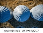 Three metal grain silos are shown in the image, with one of them having a large, round top. The silos are all made of metal and are located in a field