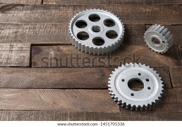 Three metal silver gears lies on old\
weathered wooden table in workshop. Copy space for\
text