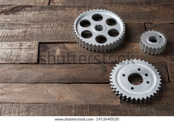 Three metal silver gears lies on old
weathered wooden table in workshop. Copy space for
text