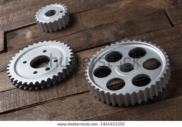 Three metal silver gears lies on old weathered\
wooden table in workshop