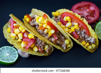 Three Mexican Tacos With Chicken Mince, Yellow Corn And Red Tomatoes And Lime Slices On Black Background