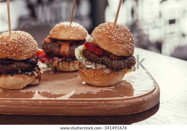 Three Mini\
Burgers Sliders On Rustic Wooden\
Plate