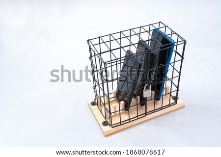 three mobile phones locked in a cage with a padlock, concept of social isolation or phone abuse and social networks, white horizontal background