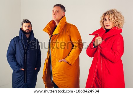 Three models on a white background in warm, winter down jackets. A group photo of two men and one woman wearing colorful clothes on a white background. Stylish winter clothes 