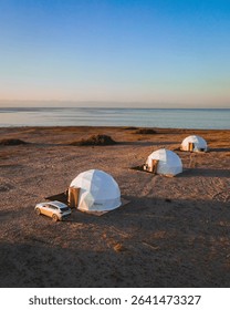 Three modern geodesic domes set on the sandy shores of Issyk Kul Lake, offering a unique glamping experience under a clear sky