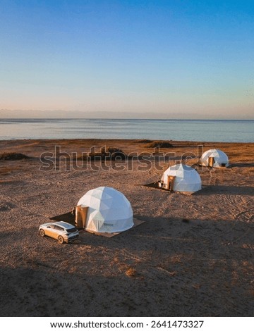 Three modern geodesic domes set on the sandy shores of Issyk Kul Lake, offering a unique glamping experience under a clear sky