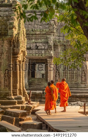 Three monks walking through the Buddhist temple of Ta Prohm within the Angkor Wat complex in Cambodia.