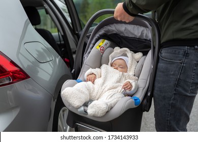 A Three Months Old Baby Girl In Car Seat Carrier Is Being Put Into The Car By His Father