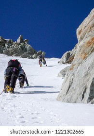 Three Mountain Climbers On A Steep North Face Heading Up A Narrow Couloir