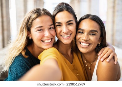 Three multi ethnic young female friends laughing together taking selfie outdoors - Multiracial women having fun on summer vacation in Italy - Unity happy people and friendship concept - Powered by Shutterstock