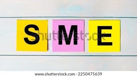 Three multi-colored paper stickers with SME SUBJECT MATTER EXPERT text on a blue wooden background.