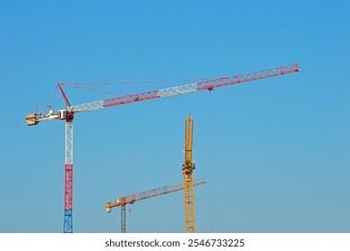 Three multi-colored tower cranes against a cloudless sky - Powered by Shutterstock