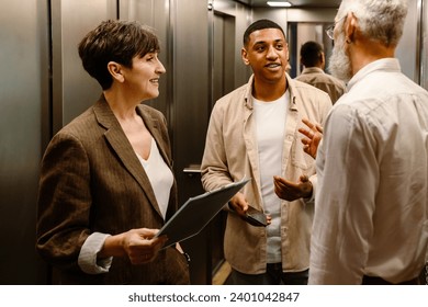 Three multicultural diverse mixed age colleagues smiling while discussing business issues in elevator - Powered by Shutterstock