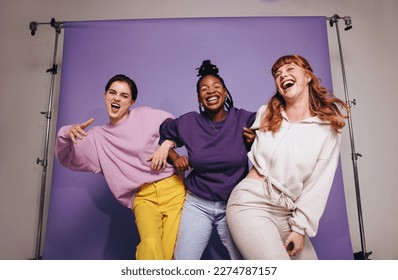 Three multicultural friends dancing and having fun in casual clothing. Group of female friends celebrating and having a good time against a purple background. Best friends making happy memories. - Powered by Shutterstock