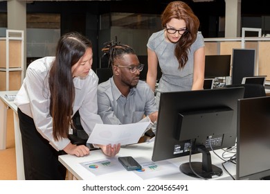 Three Multi-ethnic Business People Work Together At The Desk In Front Of The Computer In The Office