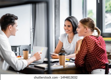 Three Multiethnic Friends Sitting At Table And Talking In Apartment  