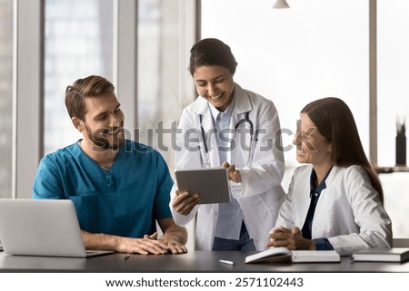 Three multiethnic medical worker using modern digital tablet device at workplace, sharing humorous, positive moment at break, read good news related to patient progress or successful treatment outcome
