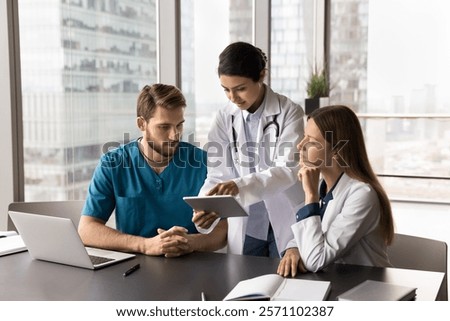 Three multinational doctors working using digital tablet, talking, reviewing patient electronic health records, analyze recent test results, medical history, medication lists, and previous diagnoses