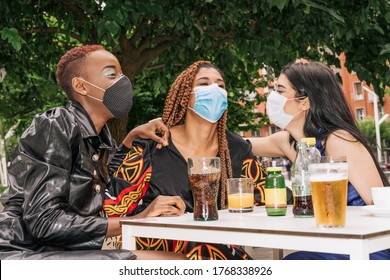 Three Multiracial, Black, Mixed Raze And Caucasian Friends On A Bar Terrace Drinking A Drink While Having Fun With Face Masks Due To The Coronavirus Covid 19 Pandemic