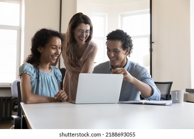 Three multiracial colleagues use laptop speaking on project, discuss collaborative task, learn new software, enjoy amusing content during break at workplace. Teamwork, cooperation, modern tech