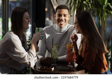 Three Multiracial Friends In A Bar Cheering. After Work Party With Cocktails After Successful Work Day.