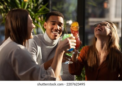 Three Multiracial Friends In A Bar Cheering. After Work Party With Cocktails After Successful Work Day.